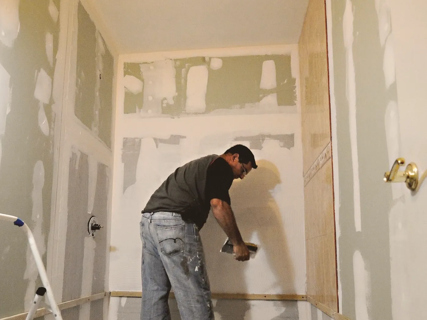 Artisan réalisant des travaux de préparation dans une salle de bain en rénovation.