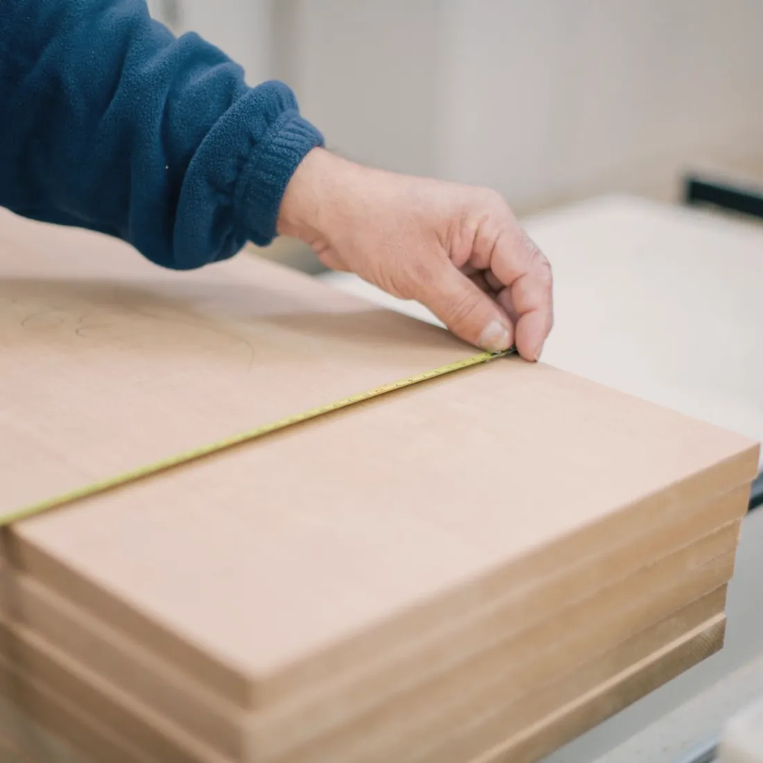 Main d'artisan utilisant un mètre ruban sur une planche de bois.